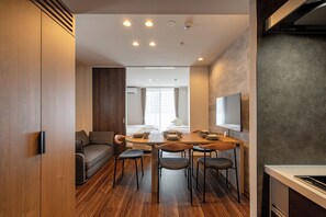 A modern hotel room with a wooden floor, a dining area with a table and chairs, a sofa, and a bed with a window view. - AIMA Asakusa East (Tokyo)