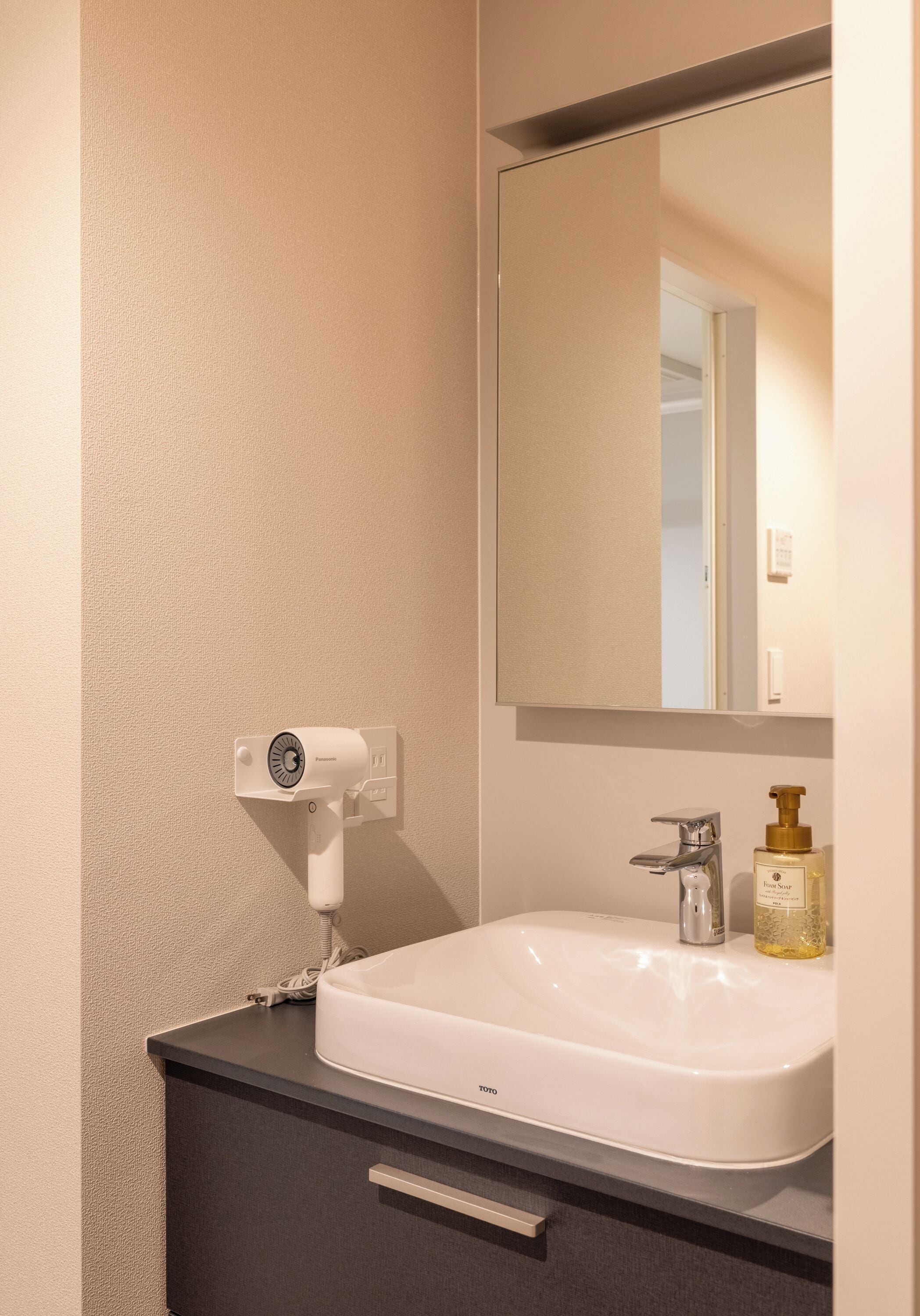 Een badkamer met een witte wastafel, een spiegel, een haardroger en een fles schuimzeep.