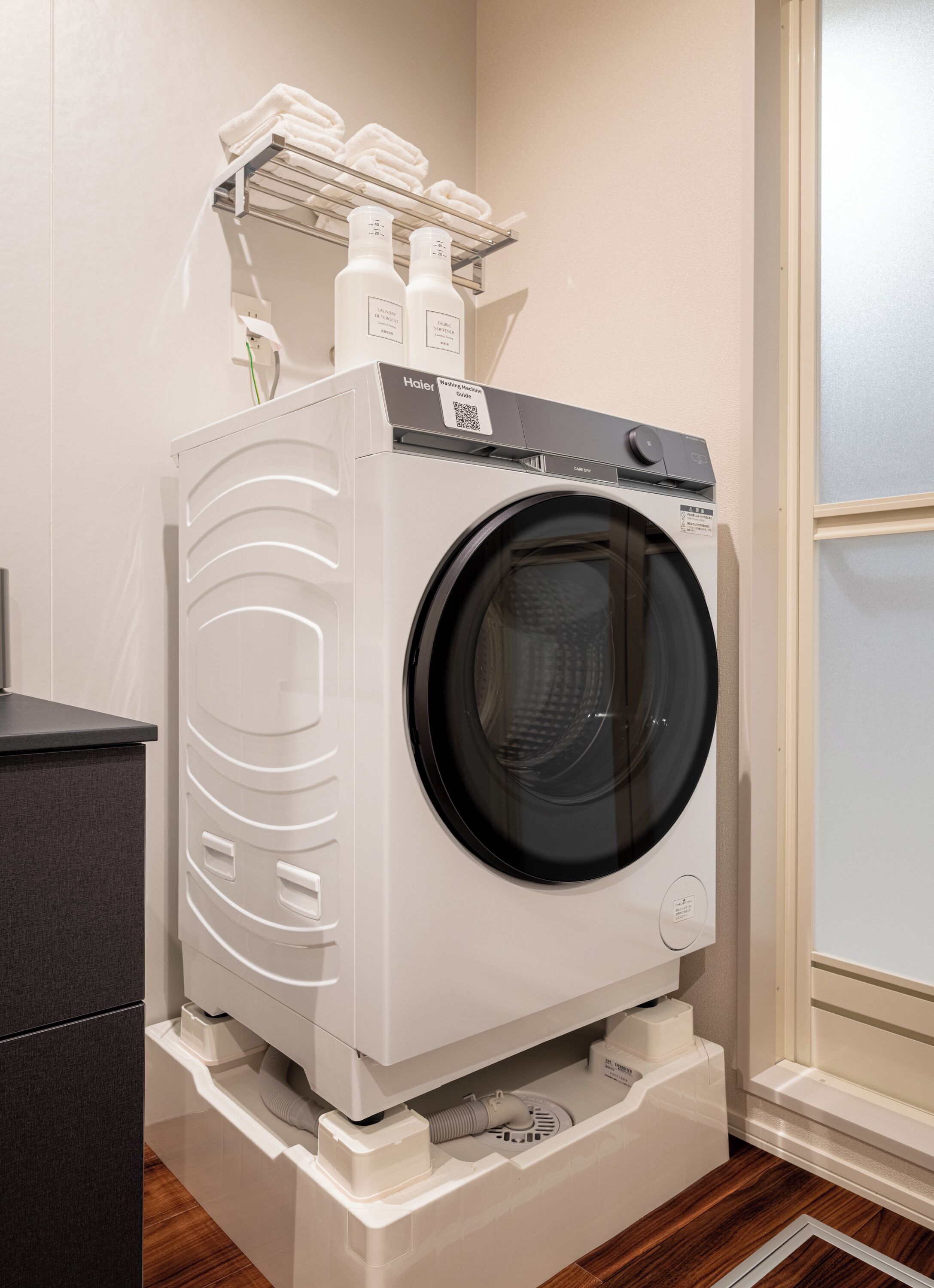 A front-loading white washer and dryer unit with a control panel, a QR code, and a shelf above for towels.