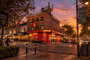 Vista de carrer al capvespre, amb un bar Liquorland ben visible i un restaurant grec de menjar ràpid i cafeteria al costat.
