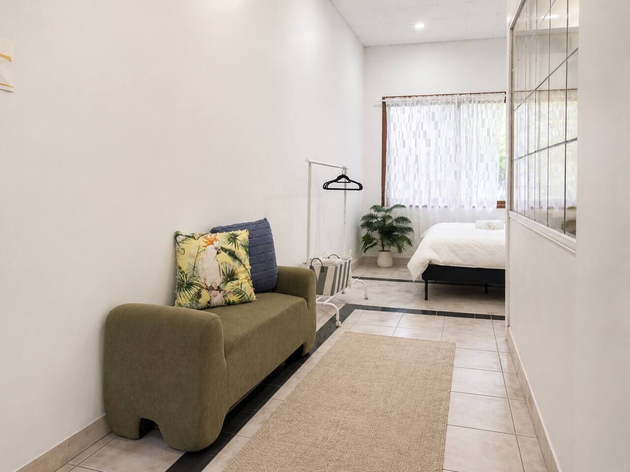A compact living space with a sofa, a bed, a hanging light, and a potted plant.