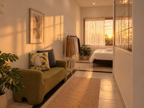 Una habitación con sofá, cama, ventana con cortinas, planta y un cuadro en la pared.