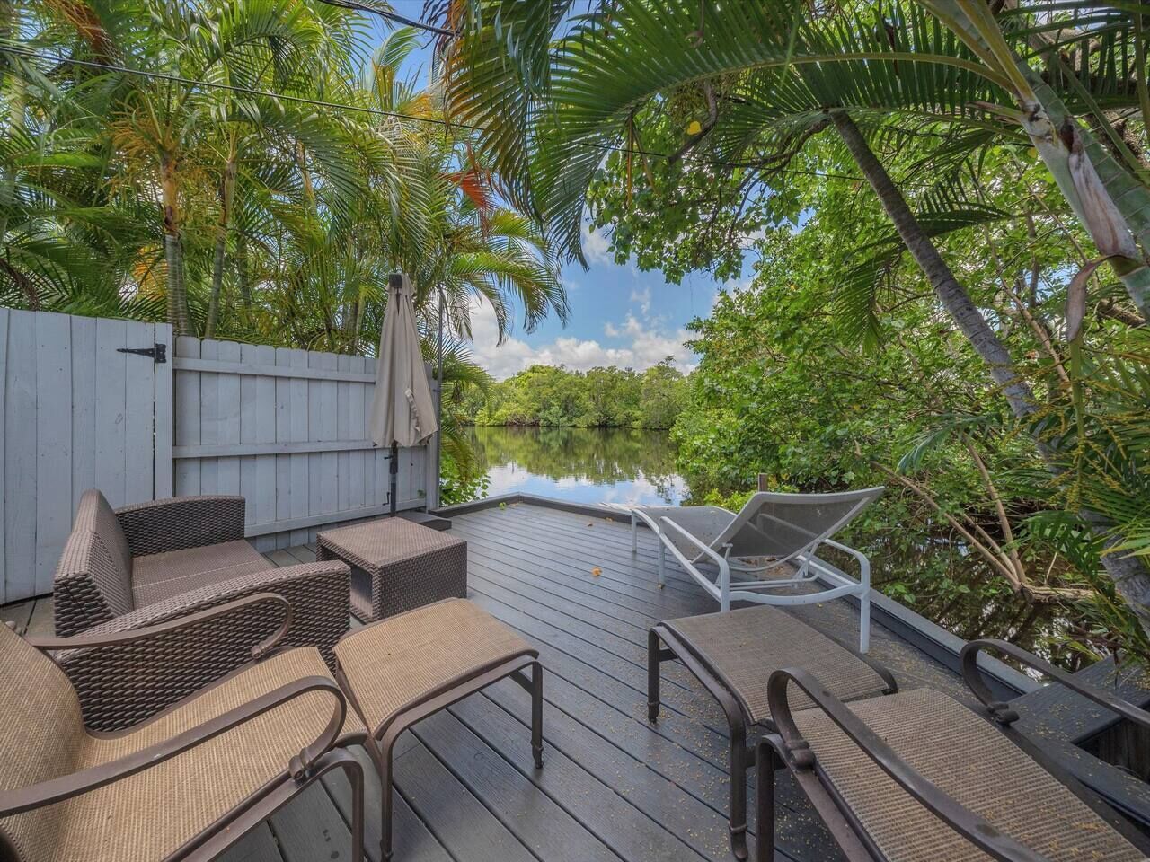 An outdoor deck with wicker furniture and a view of a water body surrounded by greenery.