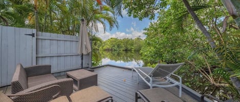 An outdoor deck with wicker furniture and a view of a water body surrounded by greenery.