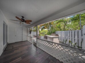 A covered patio area with a ceiling fan, a white door, and a view of a garden with a wooden fence. - Luxurious Waterfront Property with Private Lagoon (Wilton Manors)