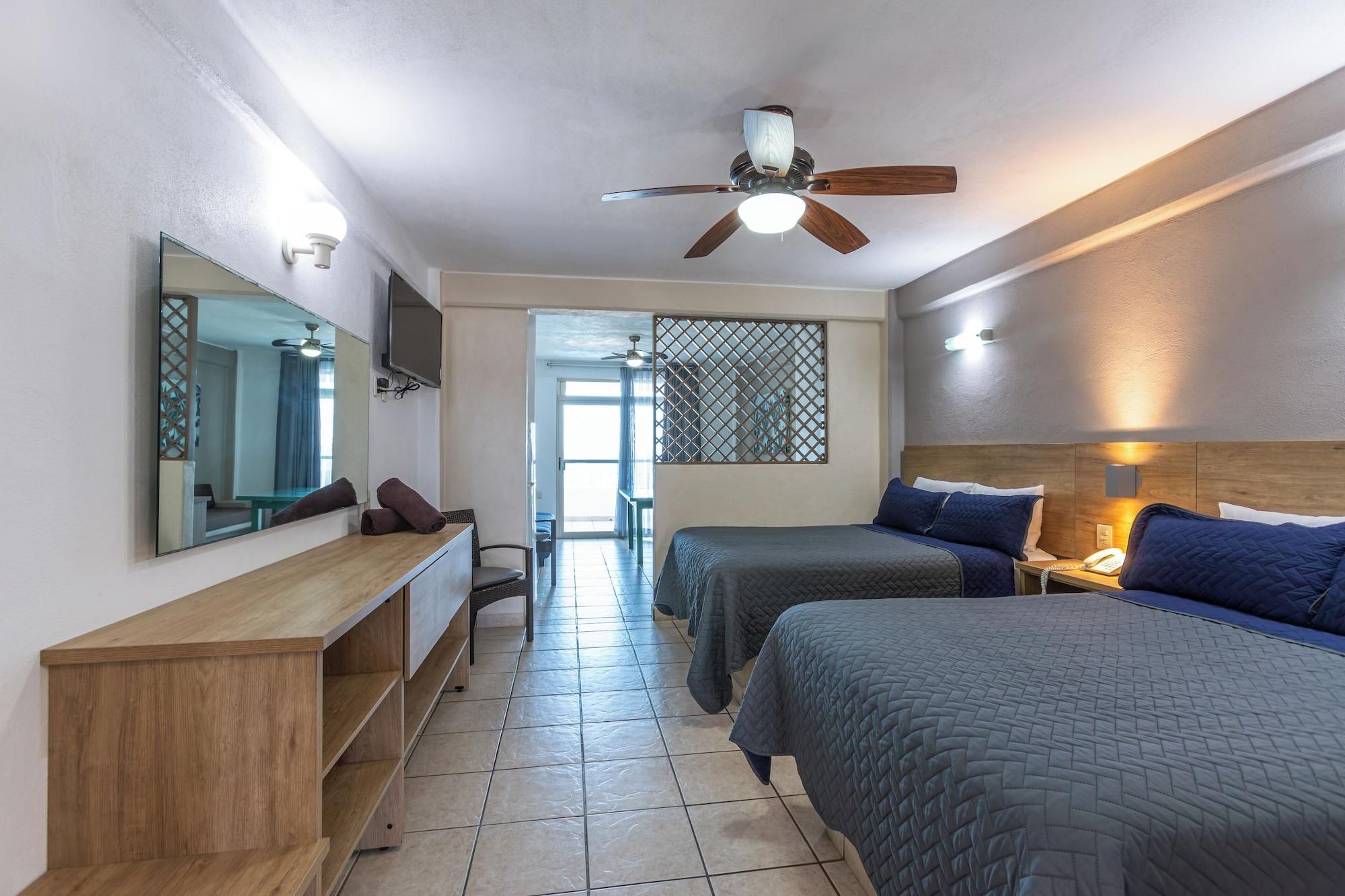 Una habitación de hotel con una cama, un escritorio, una silla, un televisor y un ventilador de techo.