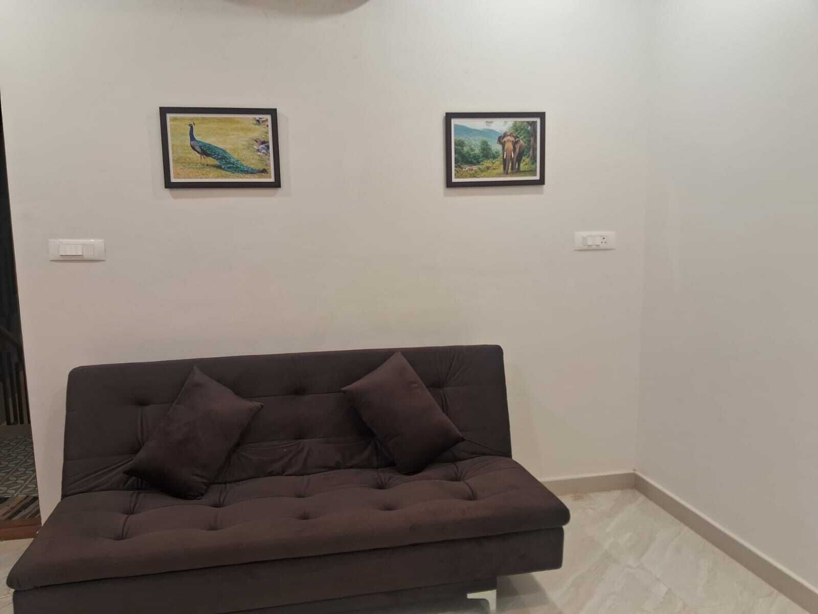 Una habitación con un sofá marrón, dos cuadros en la pared y un enchufe blanco.
