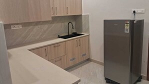 Een keuken met lichte houten kastjes, een roestvrijstalen koelkast en een zwarte kraan.