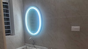 Een badkamer met een marmeren wastafel, een moderne kraan en een ovaal spiegel met verlichting aan de muur.