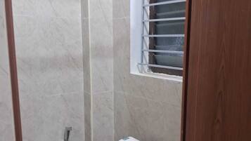 Un baño pequeño y cerrado con inodoro, zona de ducha y ventana con barrotes.