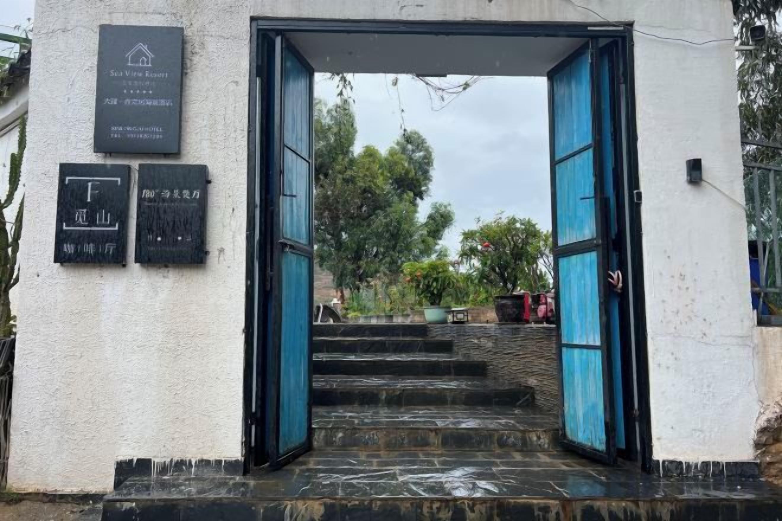 Entrada de un edificio con una puerta azul, una escalera que sube y un cartel con texto.