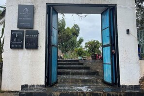 Entrada de um edifício com porta azul, escadaria e uma placa.