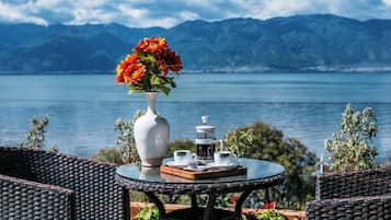 Mesa redonda con un jarrón blanco y tetera, con vista a un lago y montañas al fondo.