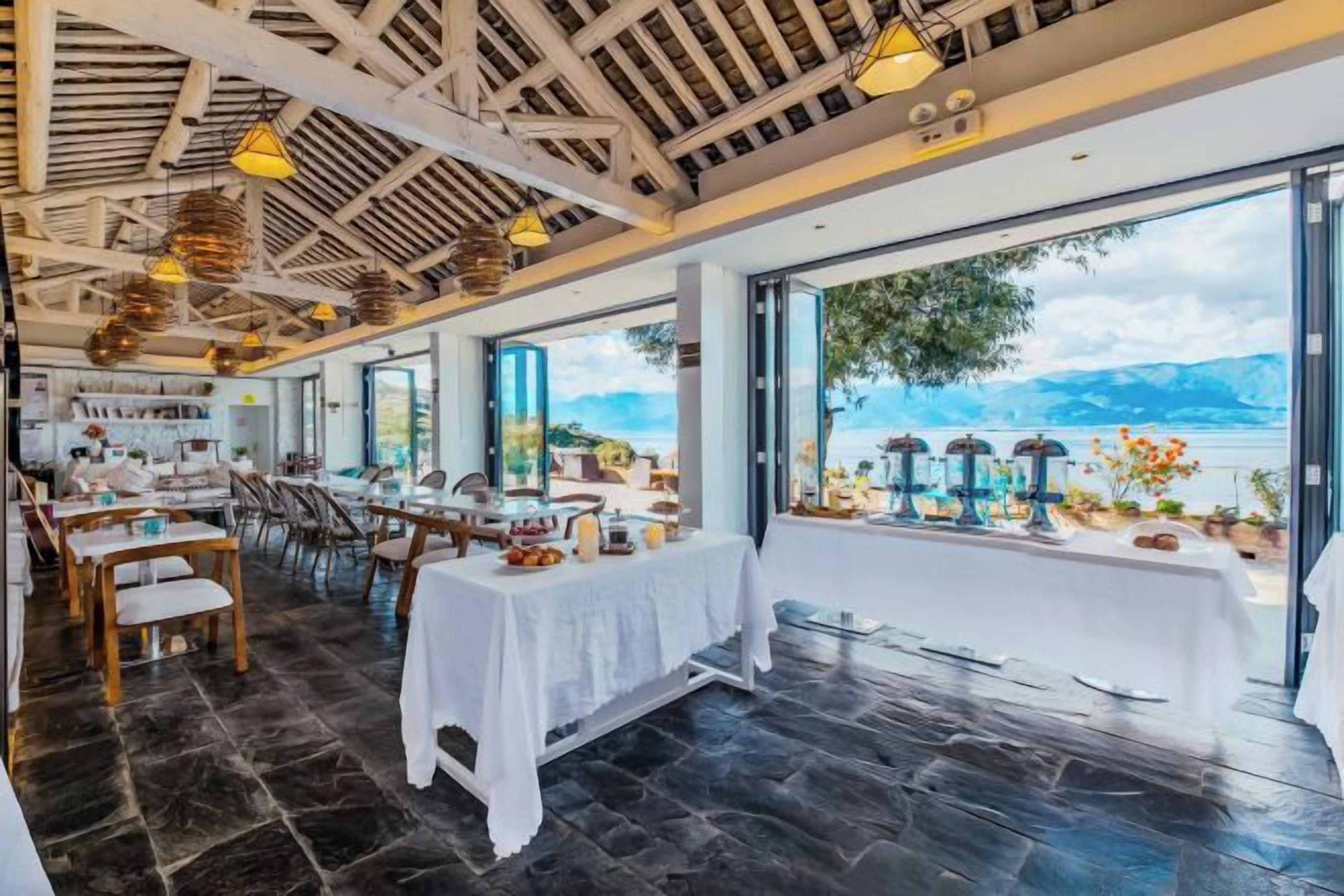 Un restaurante con terraza que da a un lago, con mesas listas para comer y vistas del paisaje.