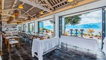 Un restaurante con terraza que da a un lago, con mesas listas para comer y vistas del paisaje.