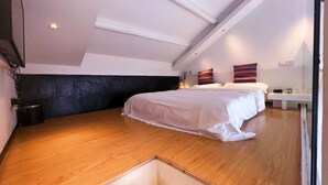 Un dormitorio con techo inclinado, una cama, una mesita de noche y una repisa en la pared.