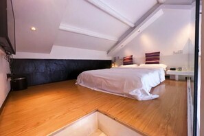 A bedroom with a sloped ceiling, a bed, a bedside table, and a wall-mounted shelf.