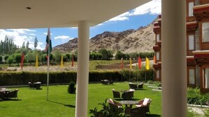 An outdoor seating area with tables and chairs, surrounded by a well-maintained lawn and a mountain backdrop. - The Druk Ladakh (Leh)