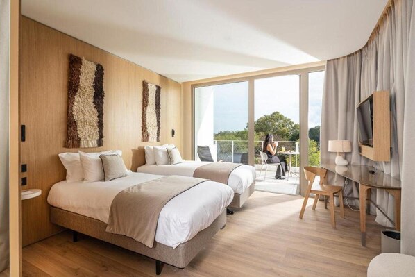A modern hotel room with two beds, a balcony, and a TV.