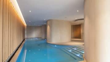 Piscina interior moderna com design curvo, rodeada por paredes com ripas verticais de madeira e iluminação embutida.