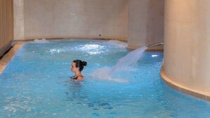 A person in a small indoor pool with a water jet feature.