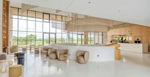 A spacious lobby with a curved reception desk, multiple seating areas, and large windows offering a view of the outdoors.