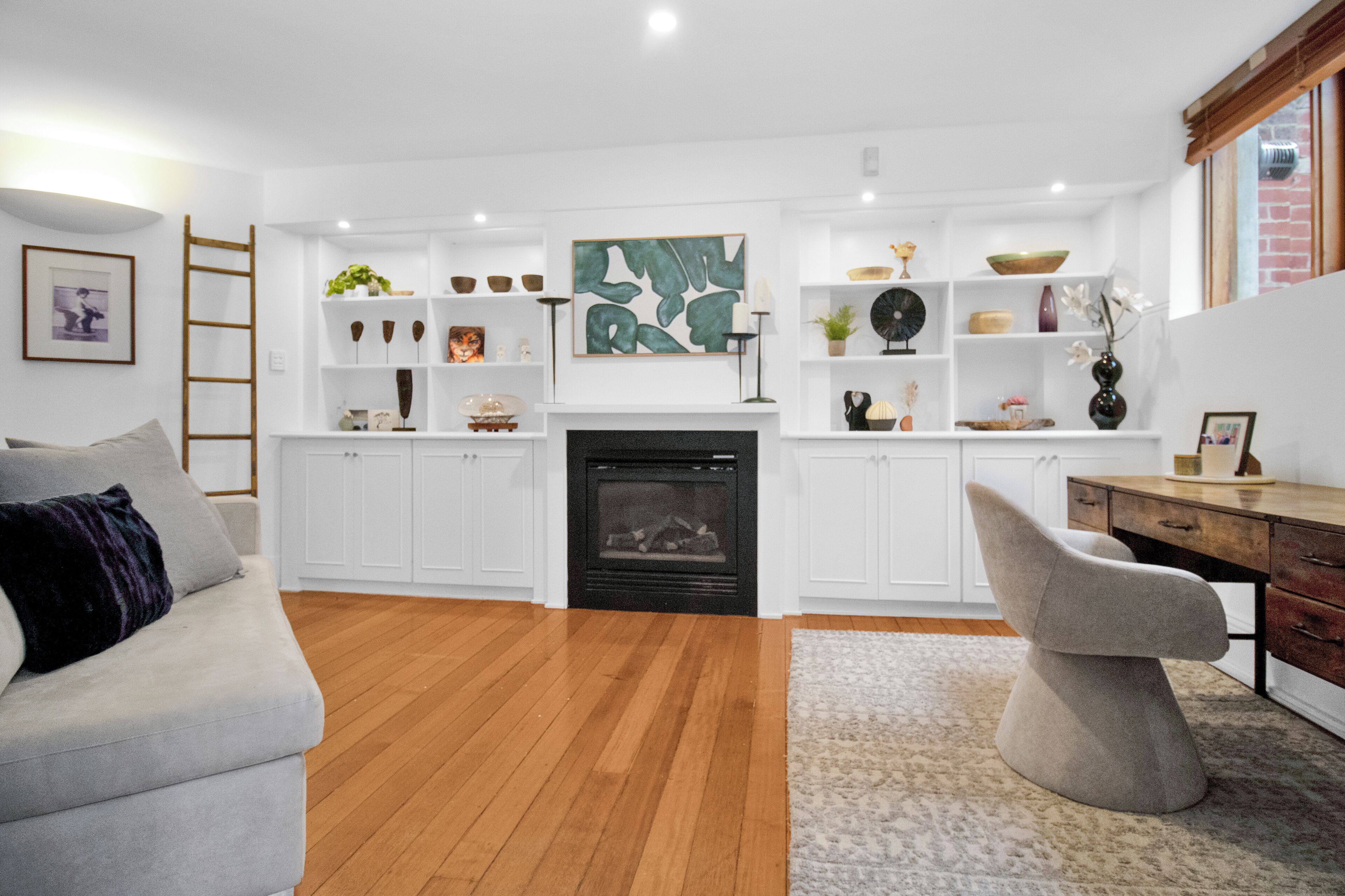 A modern living room with a fireplace, white cabinetry, and a grey sofa.