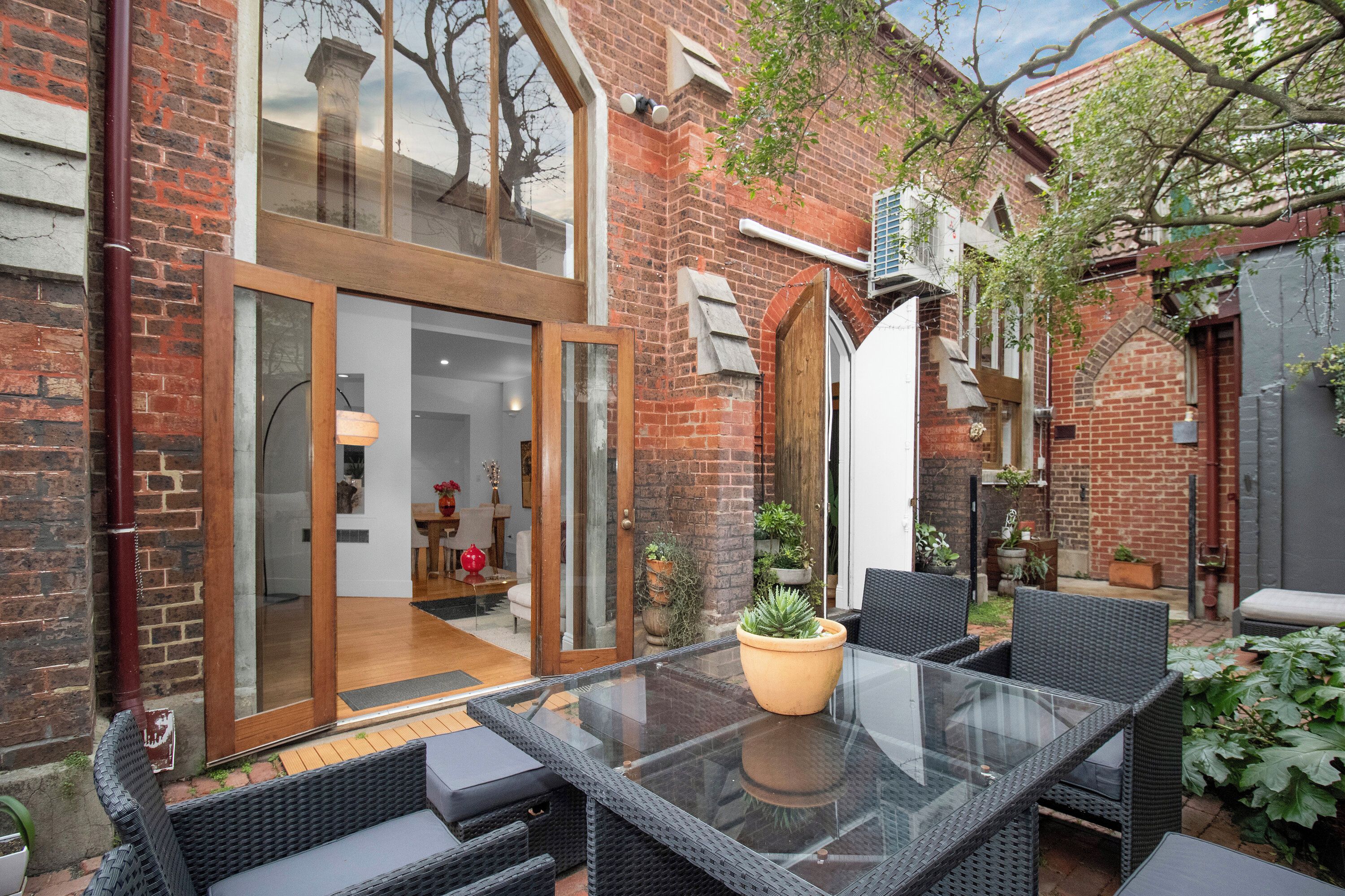 A glass-enclosed patio with outdoor furniture, a brick wall, and a door leading to an interior space.
