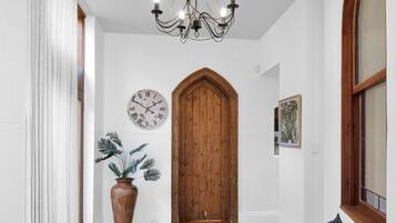 Un couloir avec un plancher en bois, un canapé bleu, une plante en pot, une porte en bois et une horloge murale.