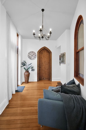 Un couloir avec un plancher en bois, un canapé bleu, une plante en pot, une porte en bois et une horloge murale.