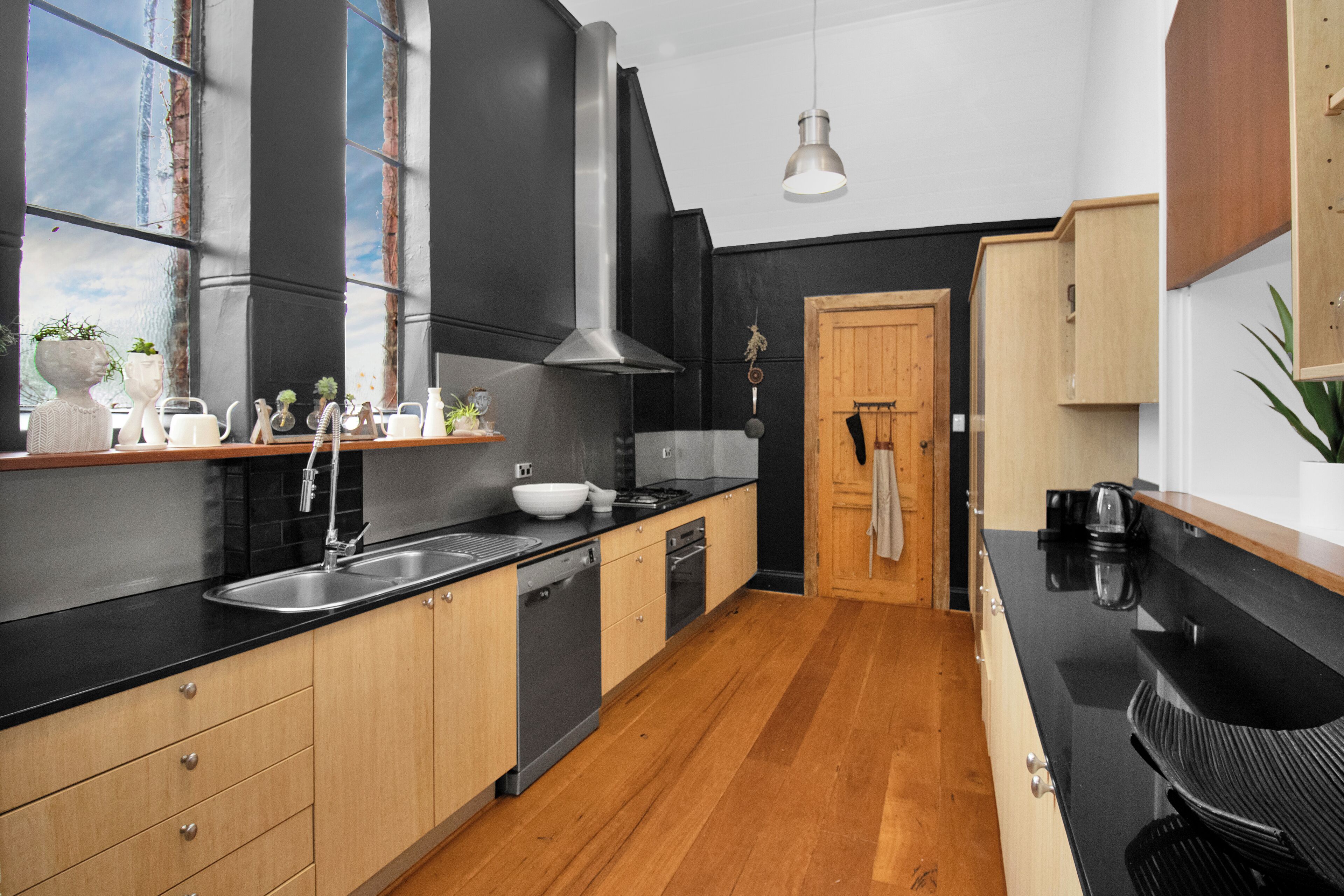 A modern kitchen with wooden cabinets, a black countertop, and a stainless steel sink.