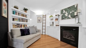 A living room with a sofa, bookshelves, a fireplace, and artwork.