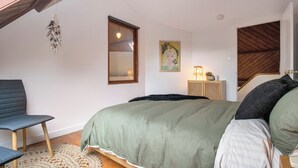 A bedroom with a bed, a chair, a rug, a painting, and a staircase.
