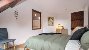 A bedroom with a bed, a chair, a rug, a painting, and a staircase.