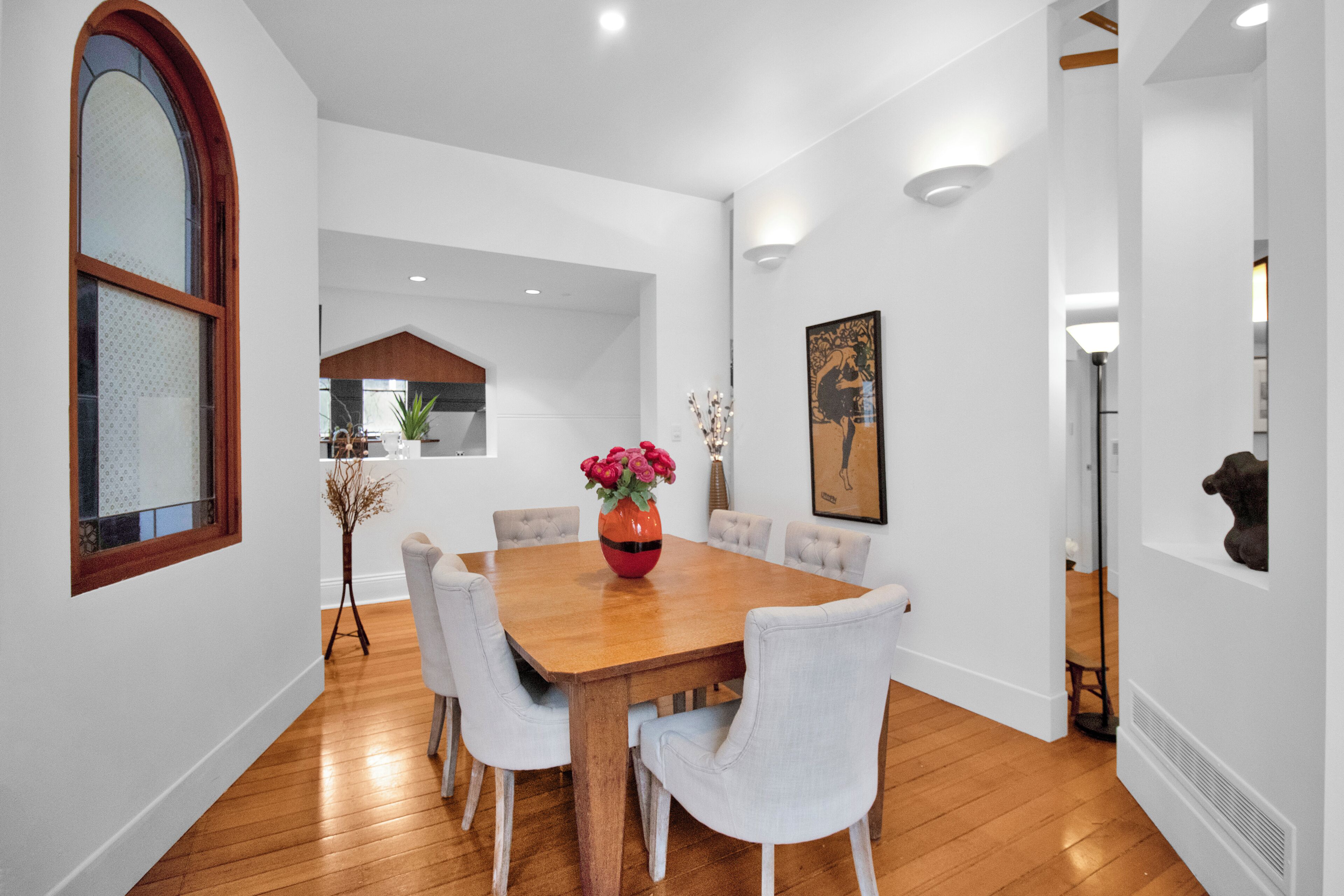 A dining area with a wooden table, six chairs, and a vase of flowers.