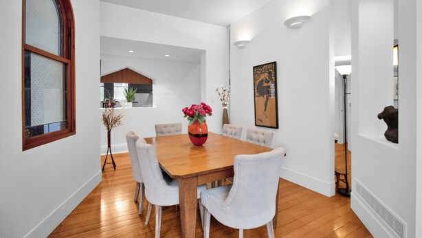 A dining area with a wooden table, six chairs, and a vase of flowers.
