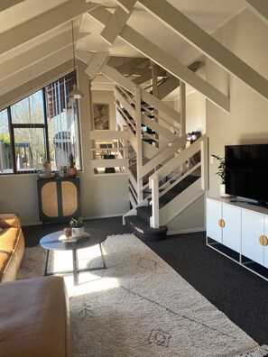 A modern living room with a staircase, a sofa, a coffee table, and a television. - A-frame with pool (Cambridge)