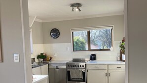 A modern kitchen with white cabinetry, a stainless steel oven, and a window with a view of trees. - A-frame with pool (Cambridge)