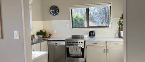 A modern kitchen with white cabinetry, a stainless steel oven, and a window with a view of trees.