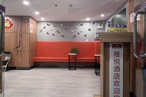 Een hotel receptie met een rode bank, een tafeltje met een plant en een wand met decoratieve details.