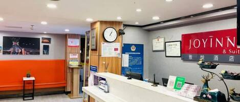 A reception area with a reception desk, a clock, and a sign for 'JOYINN & Suite Hotel'.