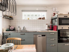 A kitchen with a dishwasher, oven, and a window with a view of trees. - Solgläntan by Interhome (Halmstad)