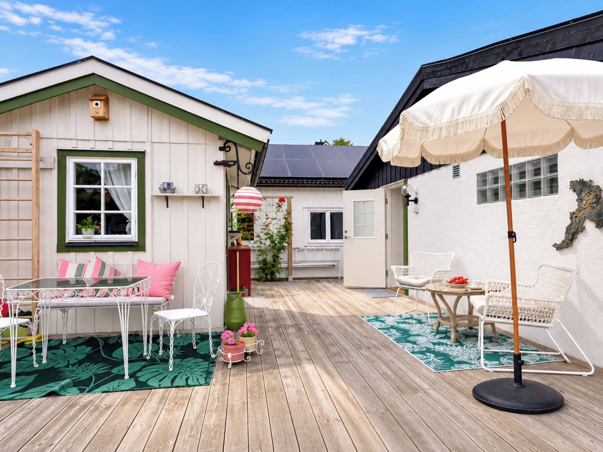 A wooden deck with a table and chairs, a white umbrella, and a small garden area with a potted plant.