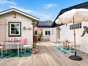 A wooden deck with a table and chairs, a white umbrella, and a small garden area with a potted plant. - Solgläntan by Interhome (Halmstad)