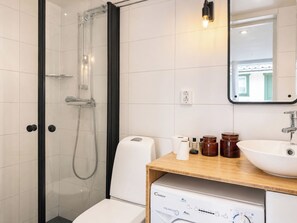 A modern bathroom with a glass-enclosed shower, a white toilet, a wooden vanity with a sink, and a mirror. - Solgläntan by Interhome (Halmstad)