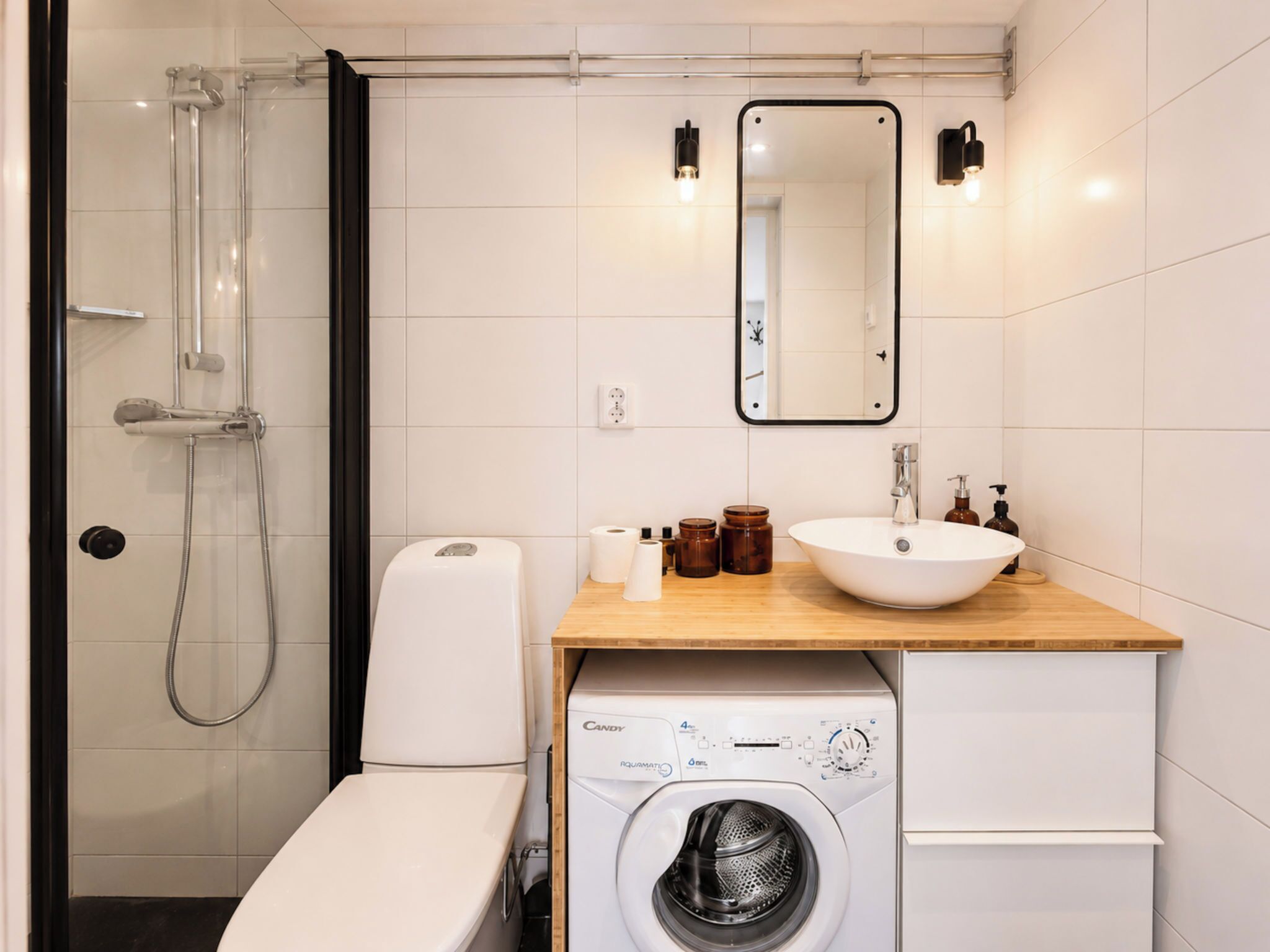 Ein modernes Badezimmer mit Duschkabine aus Glas, Toilette in Weiß, Holzwaschtisch mit Waschbecken und einer Frontlader-Waschmaschine.