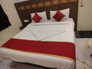 Una cama bien hecha con colcha acolchada roja y almohadas, cabecera de madera y pared blanca.
