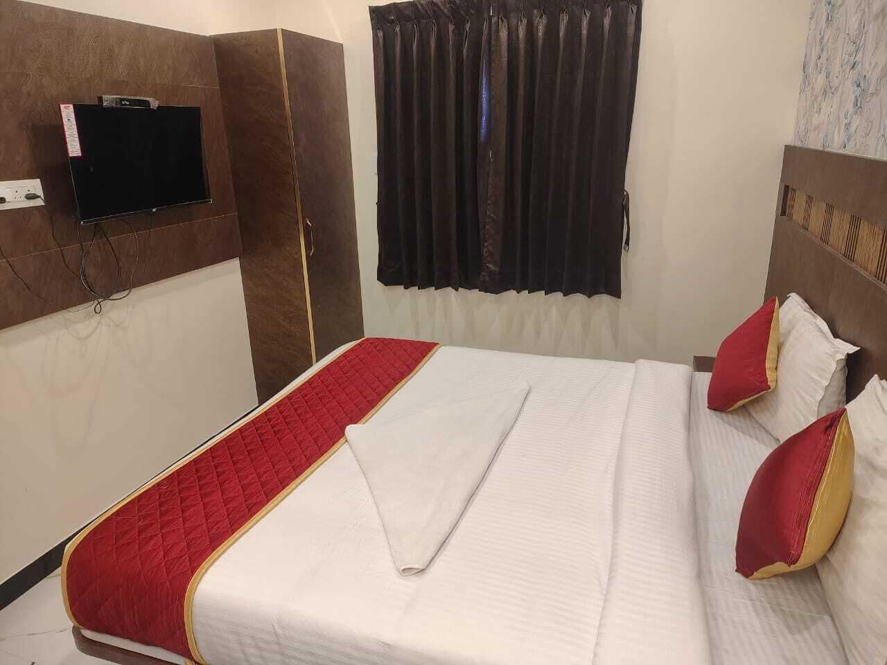 A hotel room with a bed, a television mounted on the wall, and a window with curtains.