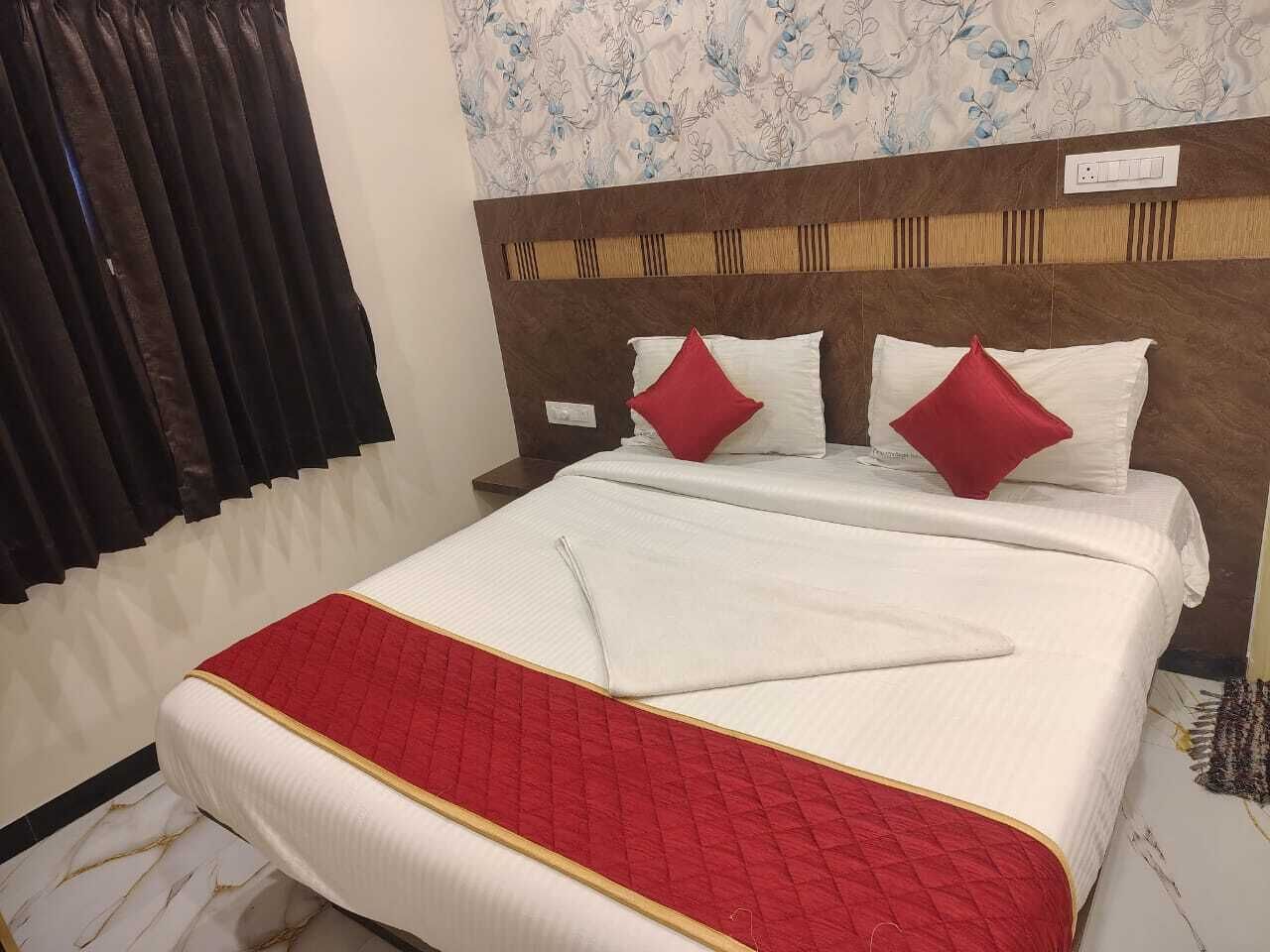Un lit bien fait, recouvert d’une couette rouge et blanche, avec deux oreillers rouges et une tête de lit en bois.