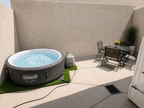 Een Coleman SALUSPA bubbelbad met een pomp, een tafel met stoelen en een potplant in een achtertuin.